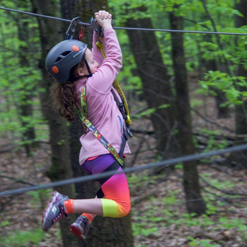 Child in helmet zip-lining through forested area.