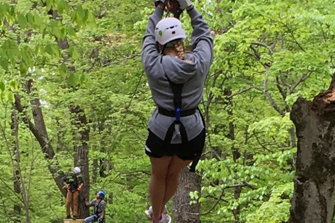 Person zip-lining through a lush green forest, wearing safety gear.