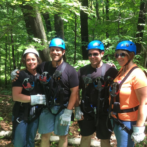 Four people in harnesses and helmets standing in a forest.
