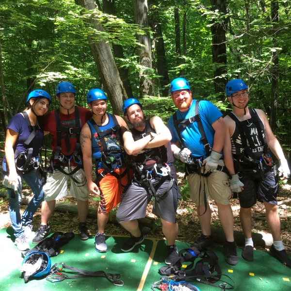 Group of six people in helmets and harnesses in a forest setting.
