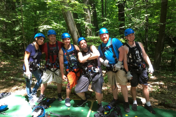 Group of six people in helmets and harnesses in a forest setting.
