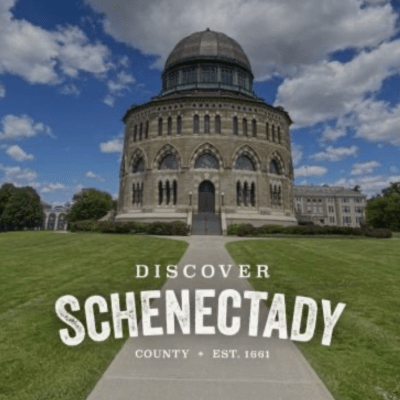 Historic dome building with cloudy sky, text 'Discover Schenectady County Est. 1661' on green lawn.