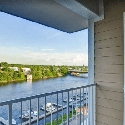 Balcony view of river with boats, dock, and trees under a clear sky.