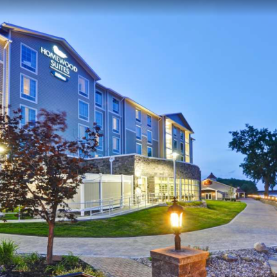 Homewood Suites hotel with pathway, trees, and river during evening.