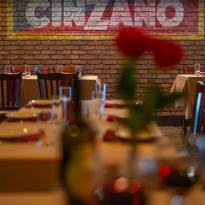 Restaurant interior with brick wall, tables, chairs, and blurred red flowers in foreground.