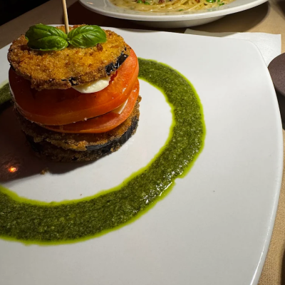 Stacked eggplant and tomato slices with pesto, beside pasta.