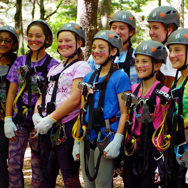 Group of smiling kids in harnesses and helmets at a ropes course.