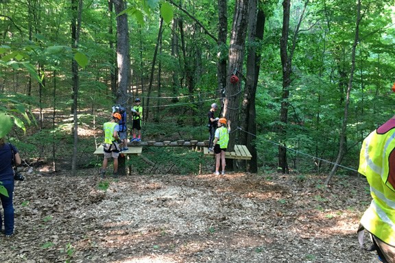 Group wearing safety gear on a treetop ropes course in forest.