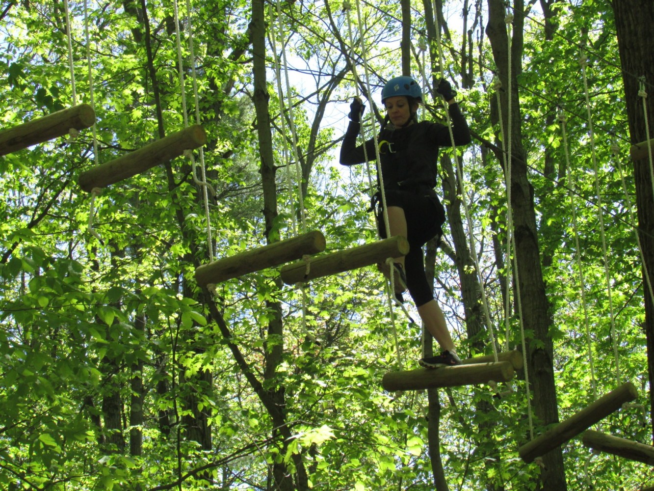 Person navigating a treetop rope course wearing helmet and harness.