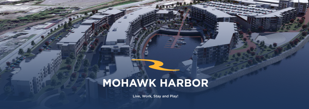 Aerial view of Mohawk Harbor, featuring buildings and a marina with the text 'Live, Work, Stay and Play!'